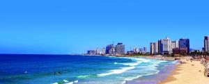 een strand met mensen die zwemmen in de oceaan en gebouwen bij Elmina Hotel Jaffa in Tel Aviv