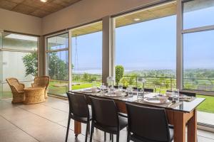 a dining room with a table and chairs and large windows at SaffronStays Serenity, Igatpuri in Igatpuri