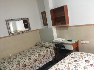 a room with two beds and a desk and a mirror at Pensión El Hidalgo in Granada