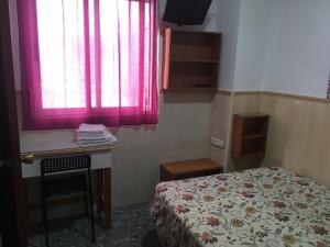 a bedroom with a bed and a desk and a window at Pensión El Hidalgo in Granada