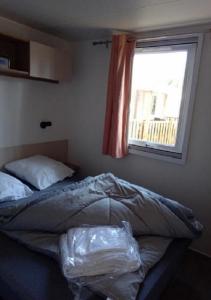 an unmade bed in a bedroom with a window at MOBILHOME SAINT JULIEN EN BORN in Saint-Julien-en-Born