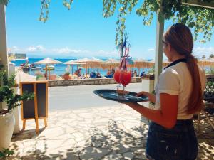 a woman holding a tray with a drink on it at Eros Beach Hotel in Benitses