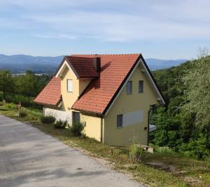 a yellow house with a red roof next to a road at Hillhouse Novo mesto in Novo Mesto