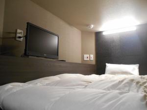 a bedroom with a white bed with a flat screen tv at BIZCOURT CABIN SUSUKINO (Male Only) in Sapporo