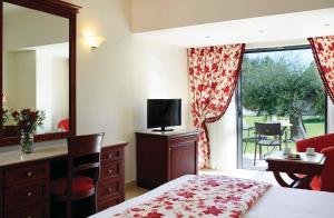a bedroom with a bed and a desk and a television at Roda Beach Resort & Spa in Karousádes