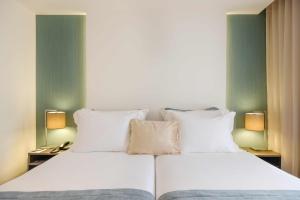 un letto con lenzuola e cuscini bianchi in una stanza di SDivine Fatima Hotel, Congress & Spirituality a Fátima