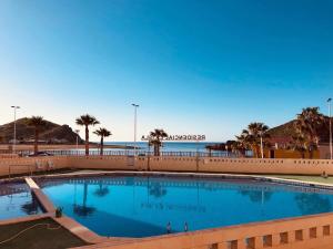 a large swimming pool next to a beach with palm trees at Apartament Claudia I in Puerto de Mazarrón