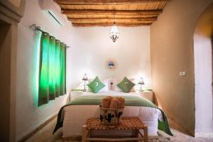 a bedroom with a bed with green curtains and a table at Riad Kasbah Aiour in Merzouga