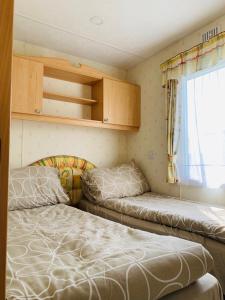 two beds in a small room with a window at Golden Sands Caravan Hire Ingoldmells- FREE in caravan wifi- Access included to the on site club house, sports bar, arcade, coffee shop We have beach access, a fishing lake and a laundrette in Ingoldmells