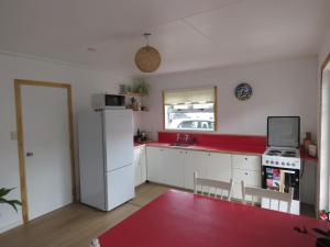 uma cozinha com um frigorífico branco e uma bancada vermelha em Pohutukawa Bach em Whangarei
