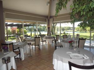 un restaurante con mesas y sillas blancas y ventanas en Les Jardins du Lac, en Trizay