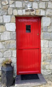a red door in a stone wall with a bucket at Turrock Cottage in Shillelagh