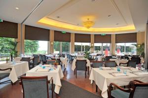 un restaurante con mesas y sillas blancas y ventanas en Fletcher Parkhotel Val Monte en Berg en Dal