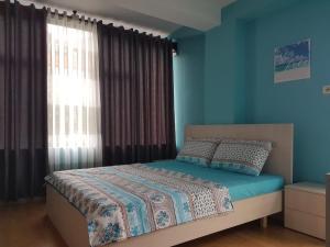een slaapkamer met een bed met blauwe muren en een raam bij Lovely Apt at the heart of the city&near the lake in Pogradec