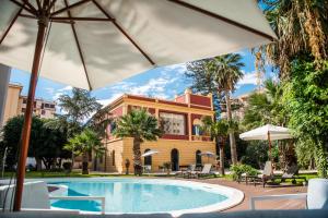 a pool in front of a building with an umbrella at Giardini Mon Plaisir in Trapani