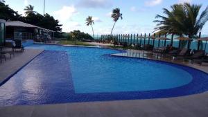 a large blue swimming pool with chairs and palm trees at Tabatinga Residence Service - Flat 02 in Jacumã