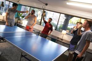 a group of men standing around a ping pong table drinking beer at Chill Backpackers in Brisbane