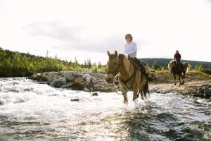 dos personas montando caballos a través de un río en Chena Hot Springs Resort, en Chena Hot Springs