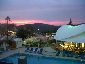 una piscina con sedie e un parcheggio con un tramonto di Ant Apart Hotel a Oludeniz