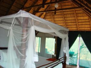een slaapkamer met een wit hemelbed en ramen bij Muweti Bush Lodge in Grietjie Wildreservaat