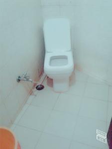 a bathroom with a white toilet in a white tiled floor at Roj Cottage in Mount Ābu