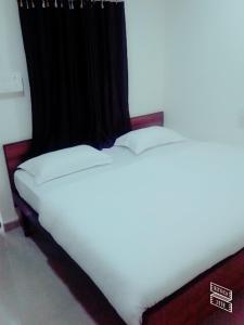 a bed with white sheets and a black curtain at Roj Cottage in Mount Ābu
