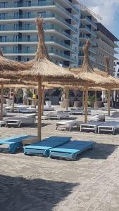 a sandy beach with chaise lounges and a large straw umbrella at Seatime Studio in primul rând la mare in Mamaia Sat/Năvodari