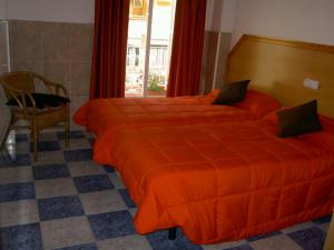 a bedroom with two beds with orange sheets and a chair at Hotel Libertador in Cullera