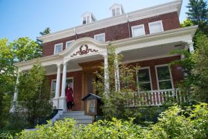 a woman standing on the front porch of a red brick house at Auberge de la Visitation in Lévis