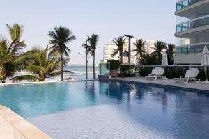 a large swimming pool with palm trees and the ocean at Lindo apartamento frente para o mar in Guarujá