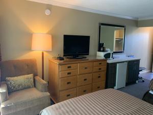 a bedroom with a dresser with a television and a chair at Okanagan Royal Park Inn by Elevate Rooms in Vernon