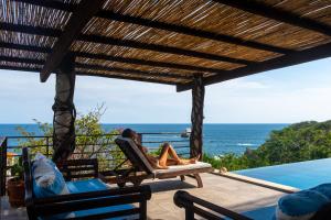 a woman sitting in a chair on a patio overlooking the ocean at Casa Kalmar in Zipolite