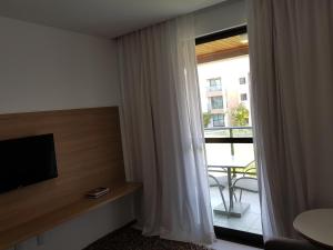 a room with a television and a window with a balcony at Iloa Residence Resort - Barra de São Miguel in Barra de São Miguel