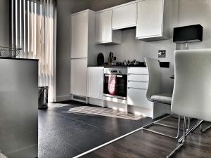 cocina con armarios blancos, fogones y sillas en Luxury 2 Bed 2 Bath Apartment 18 mins from Central London - SLEEPS 6, en Watford