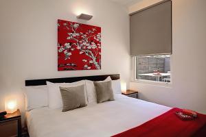 Un dormitorio con una cama blanca con una pintura roja encima. en Plum Serviced Apartments North Melbourne, en Melbourne