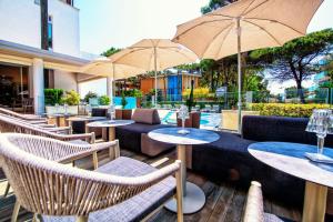 un patio con tavoli, sedie e ombrelloni di Hotel Bella Venezia Mare a Lignano Sabbiadoro