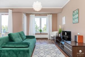 un salon avec un canapé vert et une télévision dans l'établissement Jantar Apartamenty - Family Vacation Polanki, à Kołobrzeg
