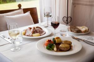 a table with two plates of food and glasses of wine at Hôtel Restaurant Le Verger des Châteaux, The Originals Relais in Dieffenthal