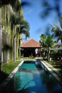 a swimming pool in front of a house with palm trees at Ganga Hotel & Apartment in Denpasar