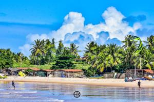 two people on a beach with houses and palm trees at Pousada Costa Prestige in Touros