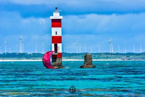 a red and white lighthouse in the water with windmills at Pousada Costa Prestige in Touros