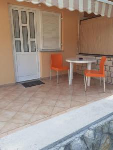 a patio with orange chairs and a table and a white table at Apartmani Ruža in Novalja