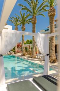 a resort pool with palm trees and white curtains at Drossia Palms Hotel and Nisos Beach Suites in Malia