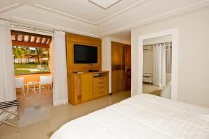 a white bedroom with a bed and a television at Hotel Ferradura Resort in Búzios
