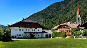 a building in front of a mountain with a church at Pension Pichler in Chienes