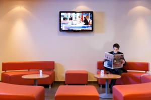 a man reading a newspaper in a waiting room at ibis Beauvais Aéroport in Beauvais