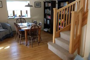 a dining room with a table and chairs and a staircase at Honey Cottage in Amlwch