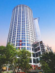 a tall white building with trees in front of it at Paco Hotel Tuanyida Metro Guangzhou -Free ShuttleBus for Canton Fair in Guangzhou