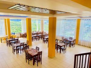un restaurante con mesas y sillas de madera y ventanas en Lourdes Hotel, en Nuwara Eliya