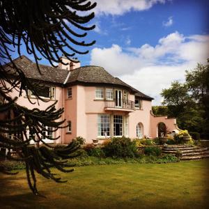 une maison rose avec un balcon sur une pelouse dans l'établissement Melfort House, à Kilmelfort